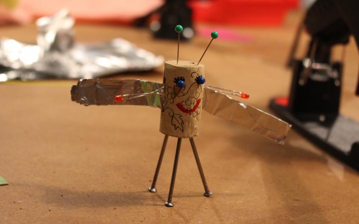 A kork, that has been turned into a little figurine with wings is sitting on a table with crafting materials around it.