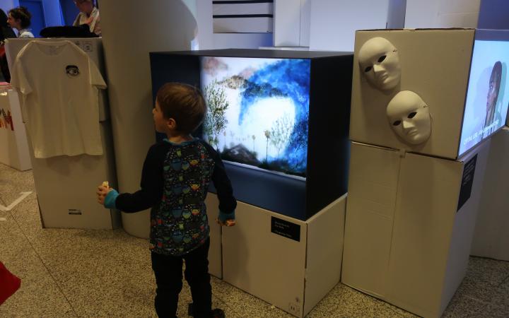 A young boy stands in front of a television set at an event of the cultural academy.