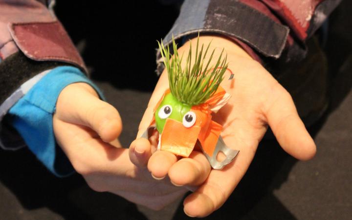 A kid is holding a little e-bug in his hands for the photo. The e-bug has fake lawn as hair and his body is made of metal and tape