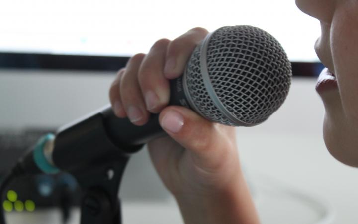 A kid is speaking into a microphone that he is holding infront of his mouth.