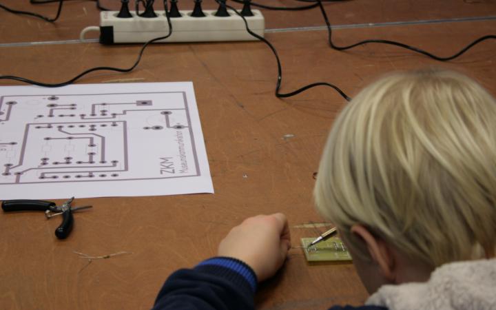 A boy is working on a circuit board with a soldering iron, out of which he is buil