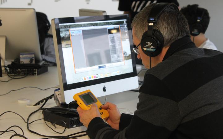 A man is composing sounds with a yellow gameboy, that he es holging in his hands.