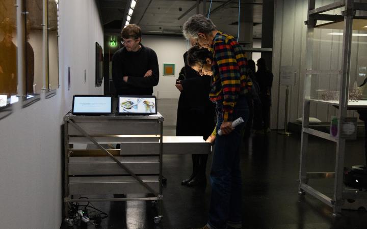 Exhibition view »Matter. Non-Matter. Anti-Matter« at ZKM | Center for Art and Media Karlsruhe, 2022. People are seen around a cart on which tablets are. Two people have opened a drawer and are looking at its contents.