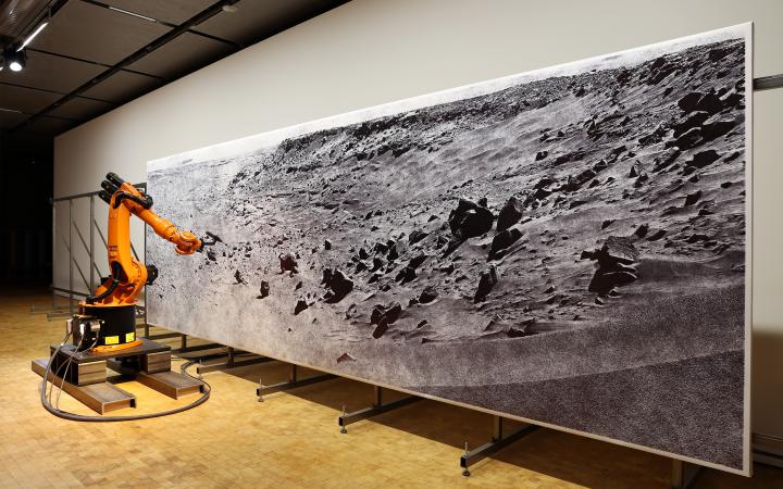 Ein orangener Roboter zeichnet ein Bild einer Mondlandschaft