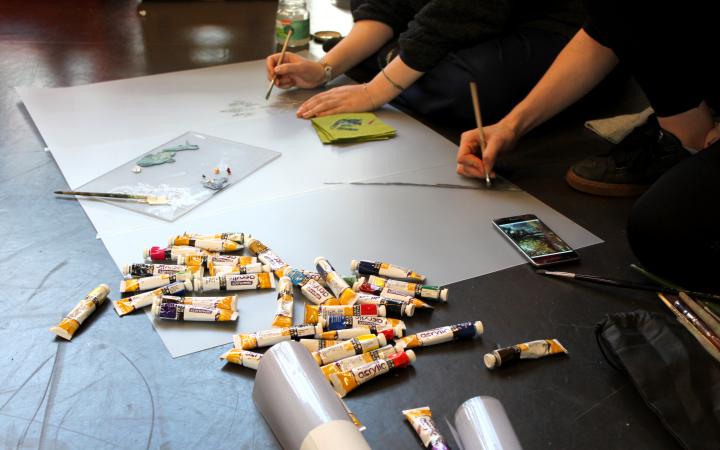Zu sehen sind viele malende Hände auf Papier und verschiedene Farbtuben im Rahmen einer Veranstaltung der Kulturakademie.