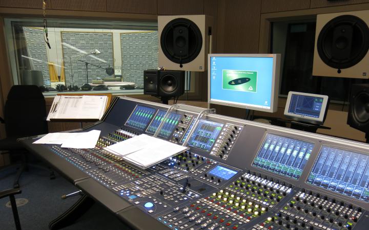 The photo shows a sound studio with mixing console and sound booth in the background.