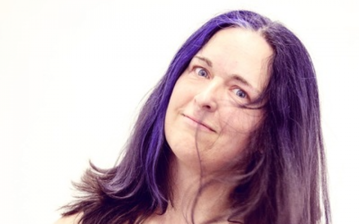 Woman with purple hair, holding her head at a slight angle.