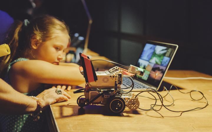 Ein Kind lehnt an einen Tisch, auf dem ein kleiner Roboter steht 