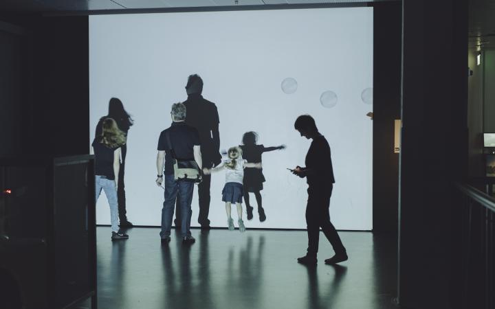Museumsbesucher bewegen sich vor einer Leinwand mit Seifenblasen 