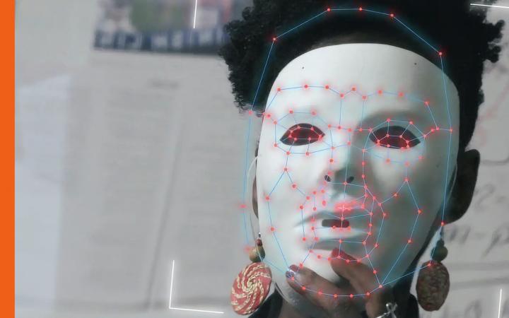 Eine schwarze Frau mit weißer Maske vor dem Gesicht. Die Maske scheint gerade von einem Computer gescannt zu werden.
