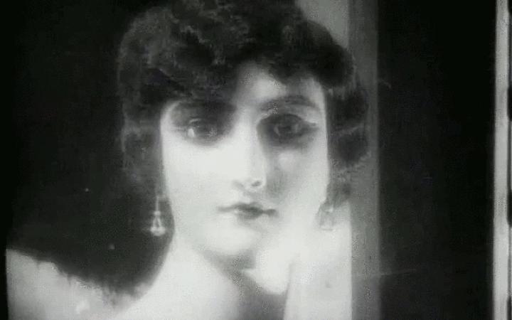 The screenshot shows a woman's profile in black and white. She looks into the camera from the front and looks almost like a doll.