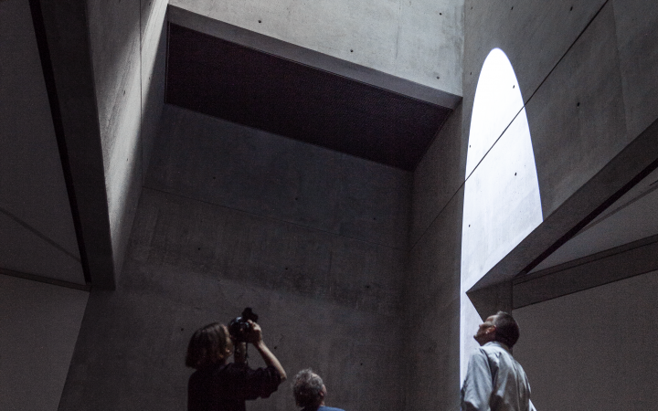 You can see 3 people in a high room with concrete walls where the sunlight shines in from above