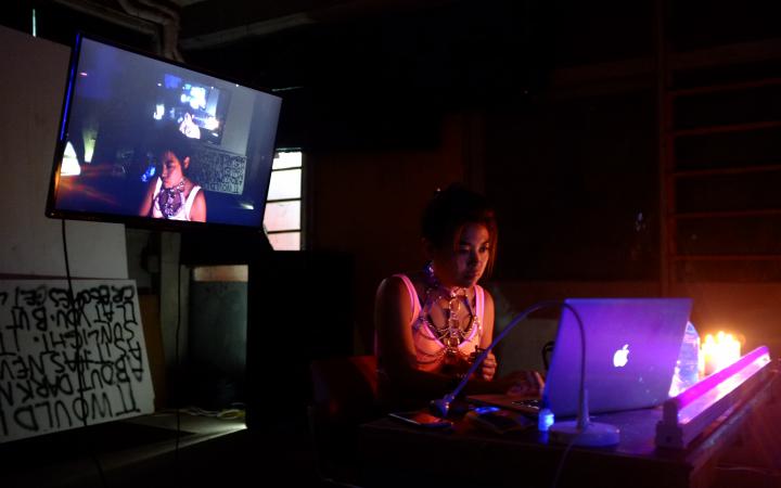 A woman sits in a dark room, illuminated by her laptop.