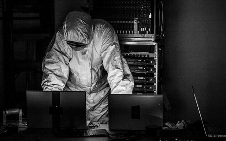 A person in a white protective suit behind a desk with laptops