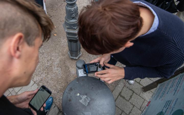 Photo of two persons using their smartphone to scan a QR code on a trash can.