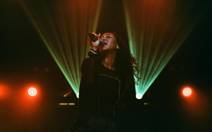 Sophia Mitiku during a performance with microphone on a dark stage with green and red light