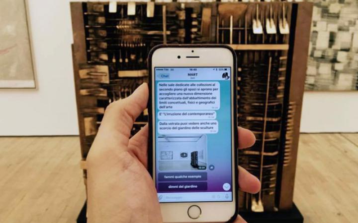 Smartphone in the hand of a museum visitor, with chat messages from the Bot Mart, in front of an artwork in the museum