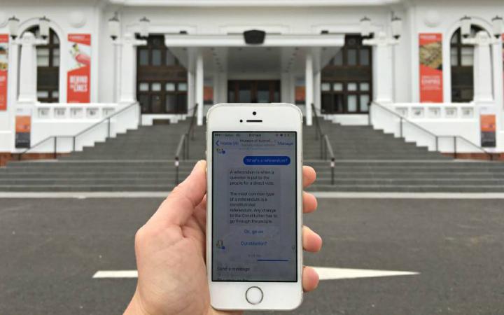 Eine Person mit Smartphone steht vor dem Old Parliament House und nutzt den Chatbot des Museum of Australian Democracy 