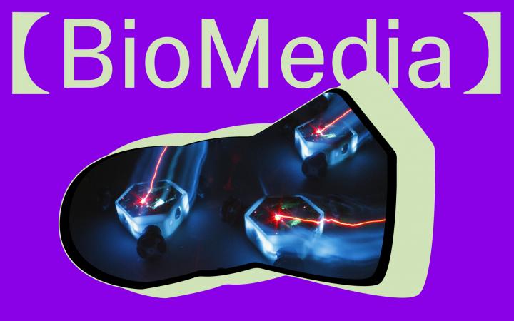 Die Grafik mit lila Hintergrund zeigt als Ausschnitt leuchtende kleine Roboterkreisel bewegen sich auf dunklem Untergrund. Darüber steht in blassem grün der Titel "BioMedia".