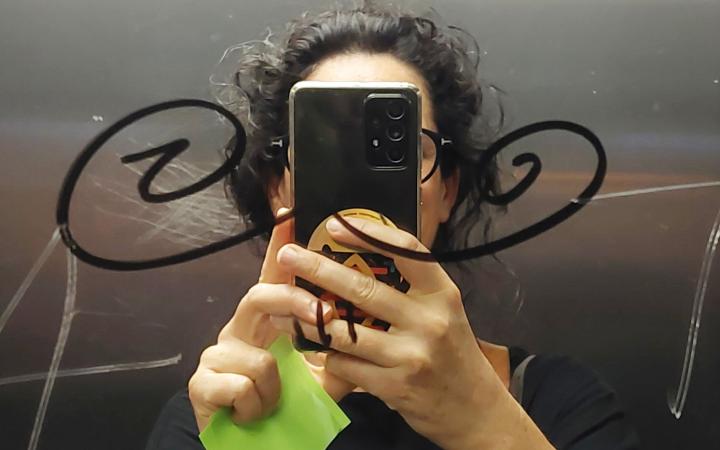 zu sehen ist eine dunkelhaarige Frau, die ihr Handy vor dem Gesicht hält und in einem Spiegel ein Selfie von sich macht.