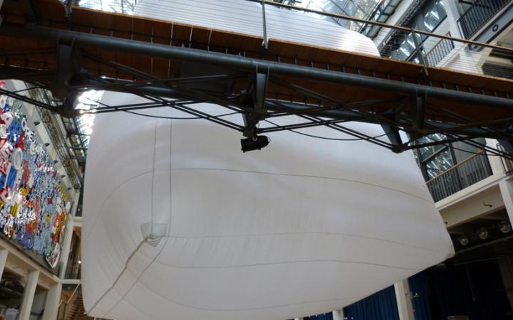 A very large white Baloon is hanging in an atrium