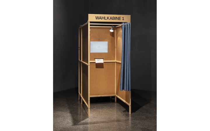Wahlkabine aus Holz, darin ein Bildschirm