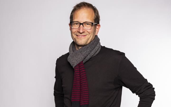 stehender lächelnder Mann mit Brille und grauem Schal