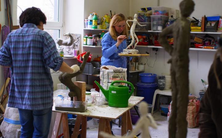 Women in an atelier are workig on slender figurines out of gesso.