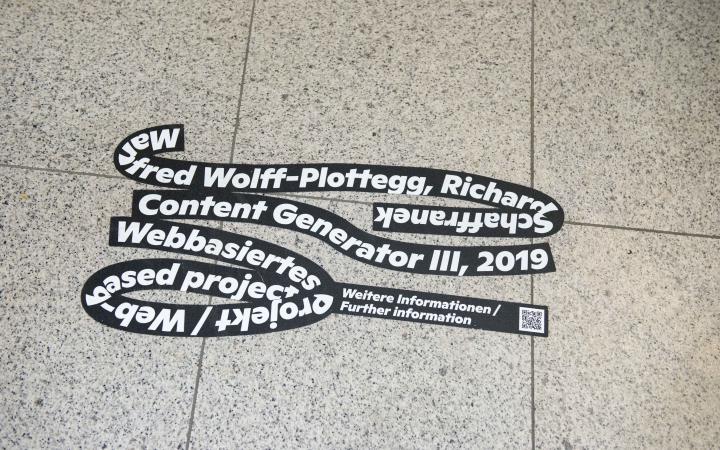 Auf einem gefließten Boden klebt die schwarze Schlaufe der Ausstellung »Seasons of Media Arts«, mit weißer Schrift über das Kunstwerk Content Generator III 