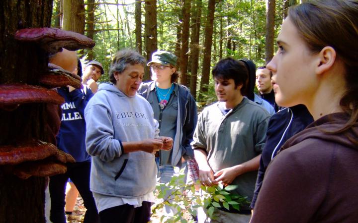 Lynn Margulis steht im Wald und erklärt einer Gruppe Studierender etwas.