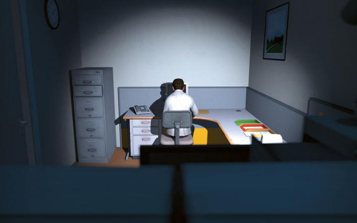 The view falls from behind on a man who is sitting at a desk in the dark
