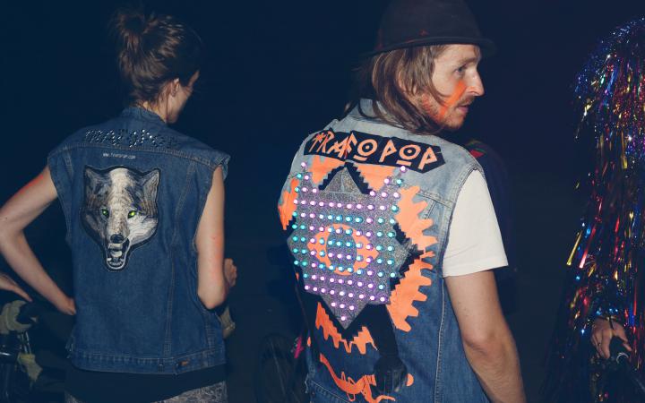 A woman and a man are standing with their backs to the observer - on their jackets there are colourful led's attached