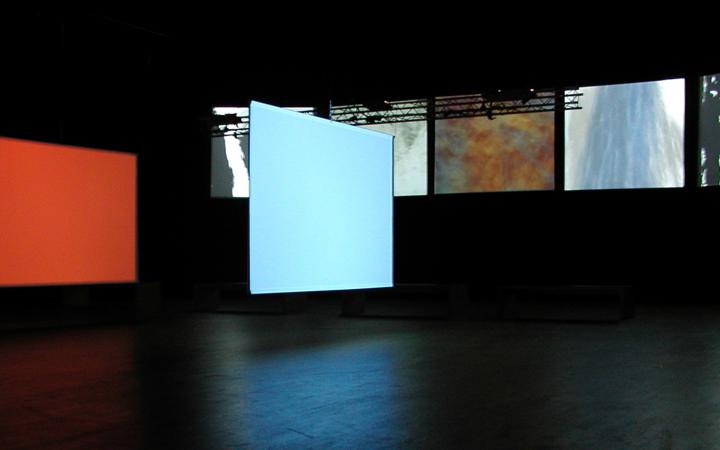  In a dark room seven screens are visible on which different abstract pictures are projected.