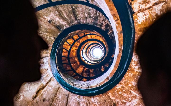 You can see a shot of a spiral staircase. On the left and right are the shadows of two heads.