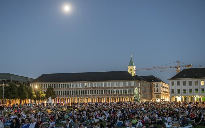 The image shows the forecourt of Karlsruhe Palace, filled with the audience of the Schlosslichtspiele