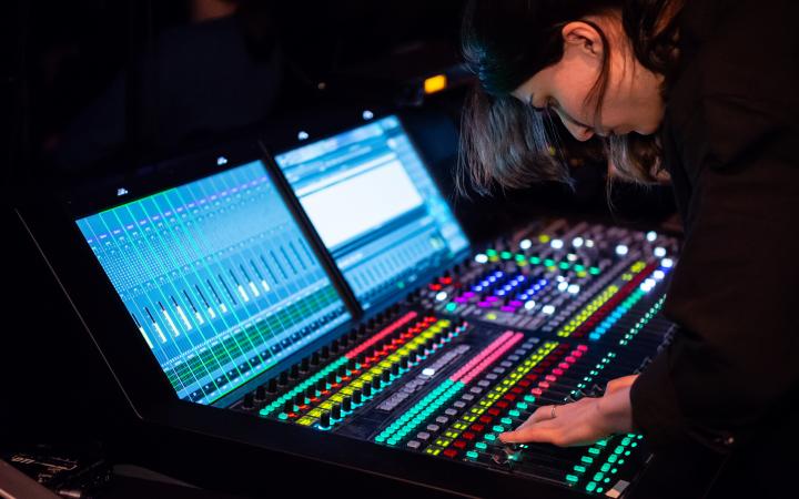 You can see a woman at a large mixing console, whose controls glow in different colors.