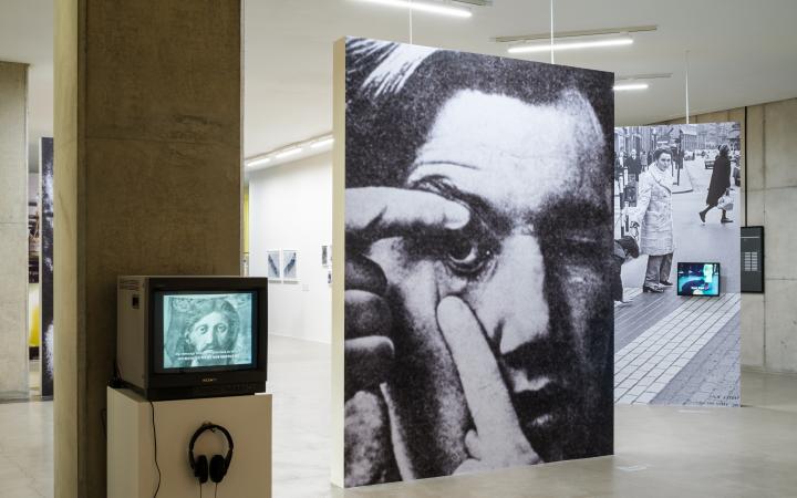 There is a black and white portrait of a person widening his eyes with the help of his fingers. To the left is a small tube TV on which video recordings are playing.