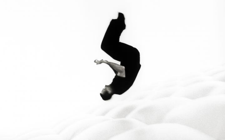You can see a person dressed in black doing a roll in the air. The background is white.