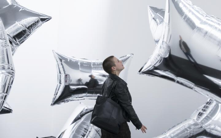 A young woman with rectangular silver balloons floating through a white room.