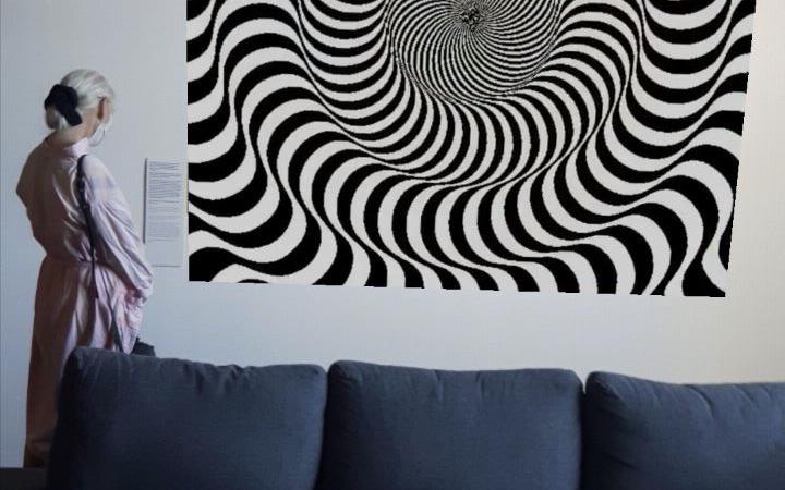 A woman stands behind a sofa, in front of a picture. The picture shows an optical illusion of black and white lines that simulate movement to the eye.