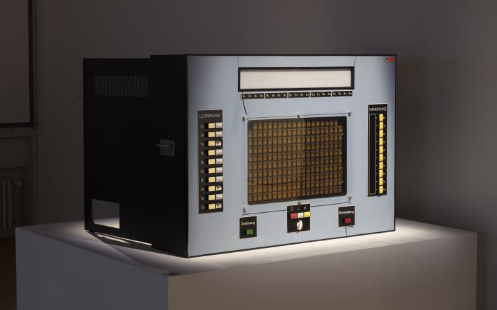 A learning computer from the 60s, rectangular, in grey and with many buttons.