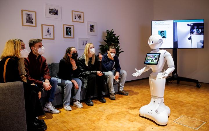 Menschen sitzen auf einem Sofa und ein Roboter steht vor ihnen