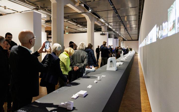 Besuchende der Ausstellung ole scheeren schauen sich die vielen kleinen 3D Drucke von geplanten Gebäuden des Architekten ole scheeren an