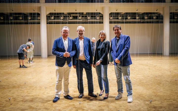 3 men, including the mayor of culture and the board of the ZKM, and a woman, the head of the cultural department of the city of Karlsruhe, stand in the atrium. William Forsythe's pendulums can be seen behind them.