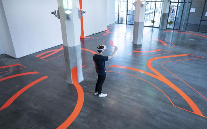 A man wears VR goggles and stands amid thick lines taped to the floor and walls.