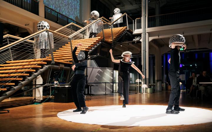 Five people in disguise dance their performance in the foyer of the ZKM. Their disguise consists of a decorated ball above their head, otherwise they are dressed in black.