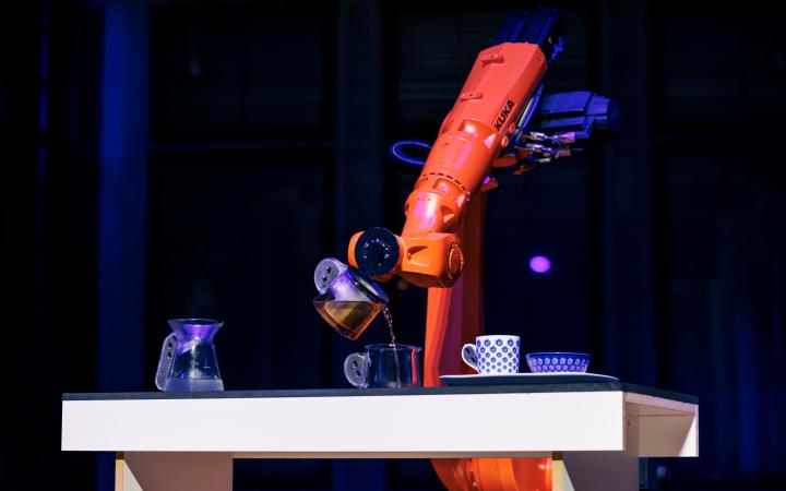 Ein orangener Roboter schenkt Tee in eine kleine Tasse ein.