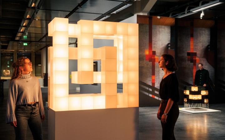 Two people look at a glowing cube riddled with holes.