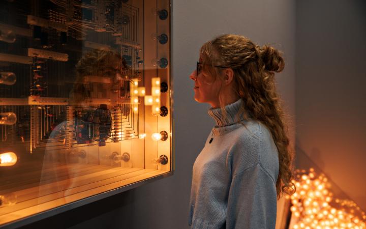 Zu sehen ist eine Person die eine Installation von Walter Giers betrachtet. Zwei der Glühbirnen der Installation leuchten.