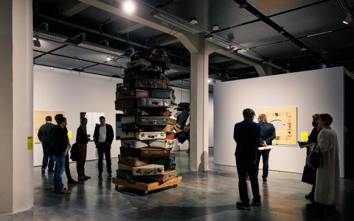 You can see several people standing around a ceiling-high stack of suitcases.